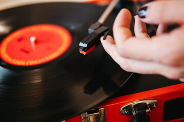 Close-up image of a person's hand placing the needle on a spinning vinyl record on a red turntable