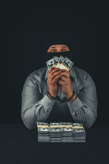 Vertical. A male businessman in a balaclava mask holds dollars in front of him and looks at the...