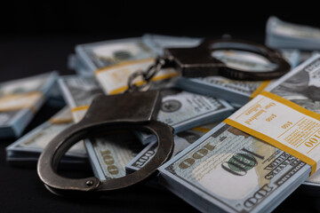 Handcuffs on packs of dollars on a black background. Packs of dollars sealed with bank tape lie with handcuffs symbolizing punishment for theft and bribery.