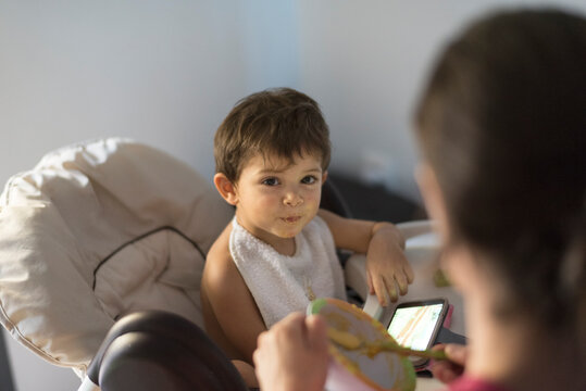 mother feeding boy who is looking phone - Powered by Adobe