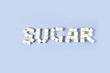 Sugar cubes lettering. Blue background. Flat lay word. Organize pile. Word shapes. Funny sweet food stack.