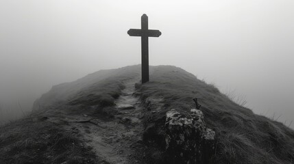   A monochrome image of a cross atop a hill against a foggy backdrop
