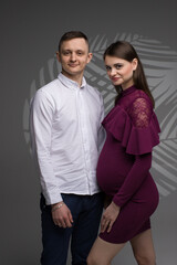portrait of a pregnancy couple, pregnant couple, pregnant woman in dress on a grey background, pregnant model posing in a studio, fashion pregnancy model
