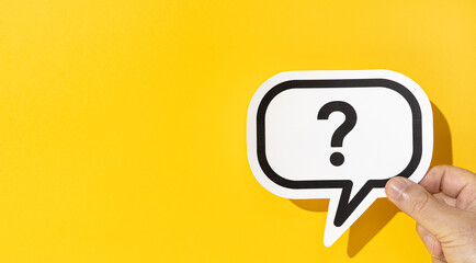 Hand holding a question mark on speech bubble on yellow background. Copy space