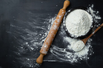 Baking background. Flour and rolling pin on dark table with copy space, top view. World Bread Day