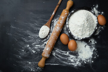 Baking background. Flour and rolling pin on dark table with copy space, top view. World Bread Day