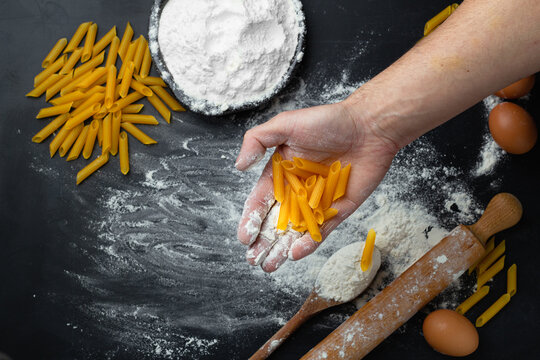 Hand holding pasta on black background before cooking. Preparing pasta. Flour on a background.