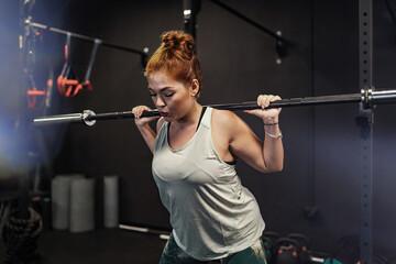 Athletic woman engaging in a strenuous gym workout, showcasing strength and determination, against a backdrop of gym equipment - Strength Training - Athletic Commitment - obrazy, fototapety, plakaty