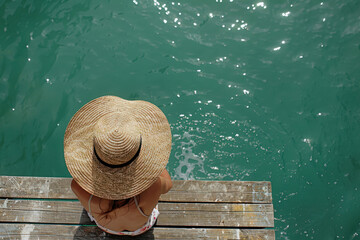 Summer holiday fashion idea: A sunbathing woman in a sun hat on a wooden pier, viewed from above