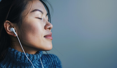 Young Japanese female model in a blue sweater with closed eyes enjoys listening to music on headphones, copy space for concept