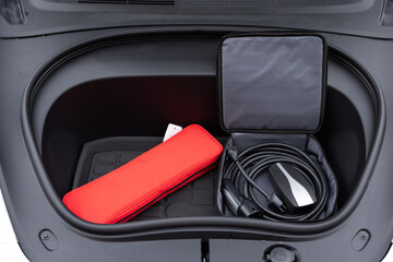 Electric car charger in car trunk. Front trunk with charging cables. Modern interior. Portable...