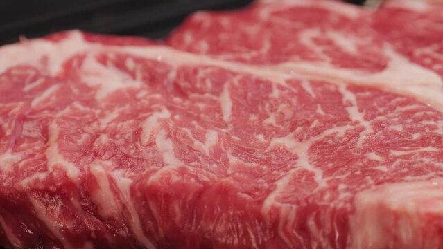 Fresh marbled beef with pepper, salt and rosemary close-up macro. Preparation to cook juicy steak on grill. Premium organic raw wagyu meat