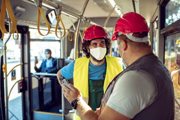 Construction workers with safety helmets and face masks talking on public bus