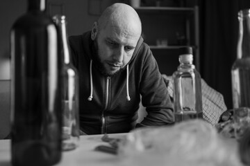 black and white portrait of alcoholic depressed man sitting near table with bottles. alcoholism, alcohol addiction and people - obrazy, fototapety, plakaty