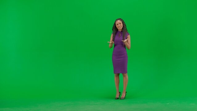 Female in dress isolated on chroma key green screen background. Full shot african american woman tv news host standing talking looking at camera.