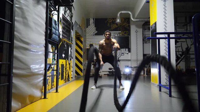 Strong african athlete training with battle ropes at fitness centre. Muscular afro american sportsman with tattoos exercising hard at modern gym. Concept of sport and active lifestyle. Close up