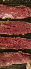 Close-up of raw steak strips seasoned and ready to cook on a dark grill pan
