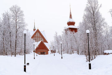 Eglise en brique rouge de Kiruna sous la neige avec une allée enneigée bordée de lampadaires en Laponie en Suède