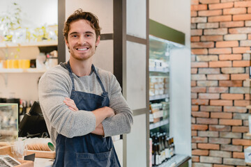 Fototapeta premium Smiling young white handsome barista standing with his arms crossed in coffee shop. Caucasian male bartender shop assistant vendor waiter looking at camera in cafeteria restaurant