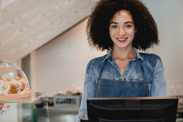 Close up photo of young african waitress working at cafe counter in coffee shop. Female vendor shop assistant barista bartender serving customers at cash point