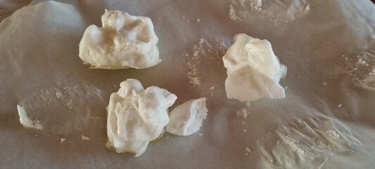 Whipped egg whites shaped into meringue drops before baking, on kitchen parchment