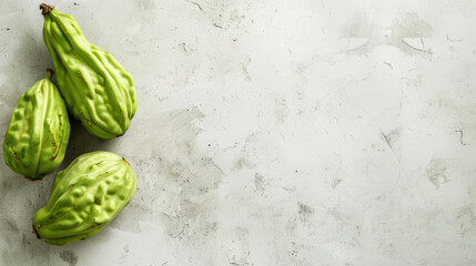 Fresh chayote squash on a white textured surface.