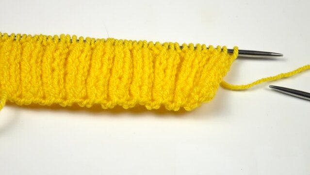 Ball of yellow threads for knitting, knitting pattern sample rib stitch, and knitting needles are on a white table