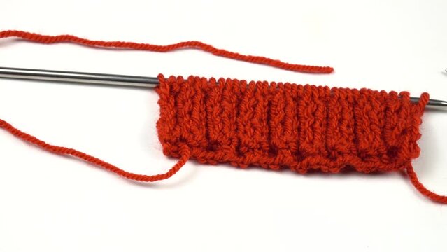 Ball of red threads for knitting, knitting pattern sample rib stitch, and knitting needles are on a white table