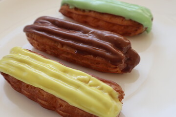 Delicious eclairs with different flavors and colorful smooth glaze on a white plate