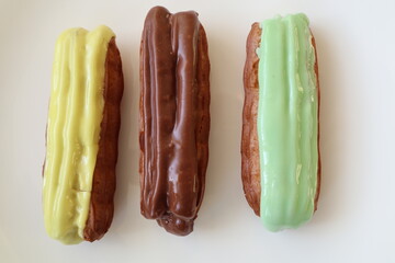 Three delicious eclairs with different flavors and colorful smooth glaze on a white plate