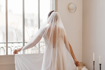 Mariée dans sa robe jouant avec son voile - 773387340