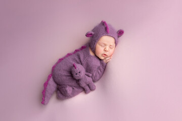 a little newly born child in a dragon costume. little dragon newborn photo shoot. sleeping child with a toy