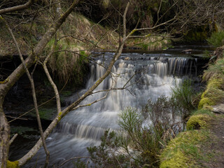 Mountain river in England, dreamy scenery, moss-covered stones and beautiful waterfall in the forest. Sunny creek in spring cloudy Yorkshire evening. small cascade surrounded by moss and autumn leaves