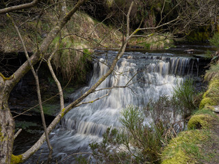 Mountain river in England, dreamy scenery, moss-covered stones and beautiful waterfall in the forest. Sunny creek in spring cloudy Yorkshire evening. small cascade surrounded by moss and autumn leaves