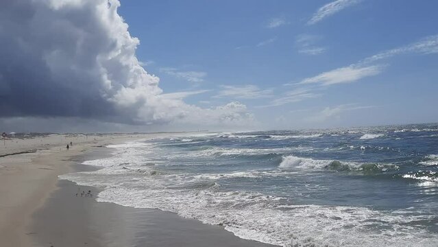Shot of ocean waves splashing the beachfront with some people walking on it.