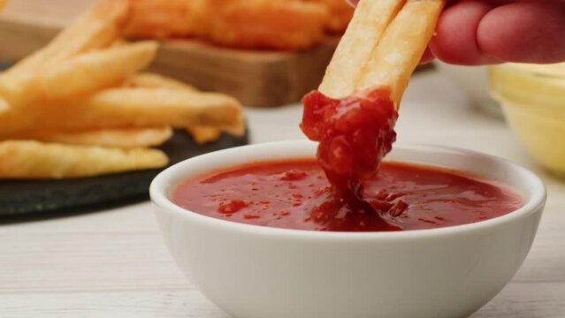 Pouring fry potato in red tomatoes ketchup sauce close-up. Eat french fries with marinara sauce. Fast and junk food concept.