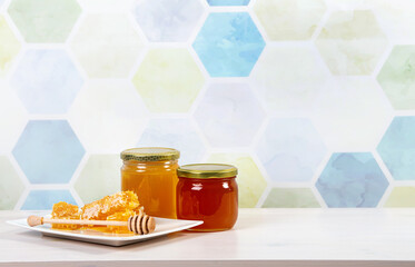 Glass honey jars with different color honey inside, lot of copy space on light blue honeycomb pattern background. Honey border background concept.