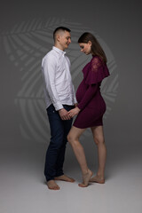 portrait of a pregnant couple, pregnant couple stands on a grey background in a studio, studio pregnancy photo shoot, pregnant woman posing in a studio, pregnant, pregnancy, maternity style