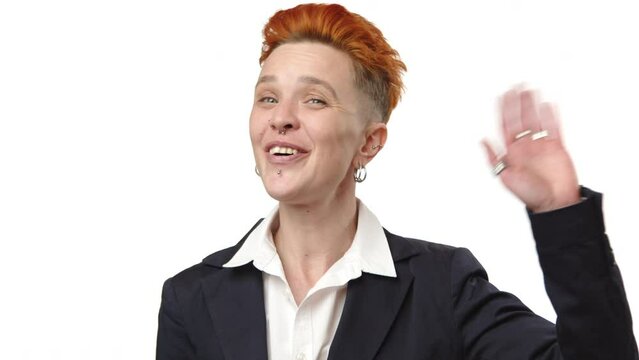 Smiling warmly, a professional woman with stylish red hair greets with a wave, signaling a welcoming and approachable attitude in her dark business suit. Camera 8K RAW. 