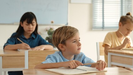 Caucasian boy looking at blackboard while diverse skilled student learning at school and taking a note. Smart child in casual cloth sitting in front of blackboard while children doing test. Pedagogy.