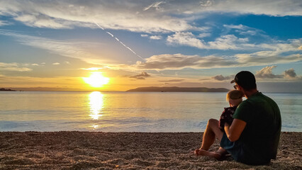 Father with small child enjoying romantic sunset at beach in town Makarska, Split-Dalmatia, Croatia, Europe. Coastline of Makarska Riviera, Adriatic Sea. Dreamlike atmosphere. Family vacation concept