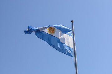 Argentine flag flying on a mast with a blue sky in the background
