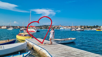 Tourist woman at red heart shaped landmark at idyllic port of coastal town Medulin, Istria...