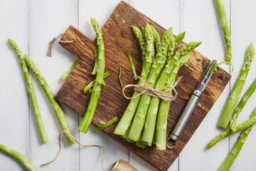 Peeling fresh green asparagus on wooden cutting board - 773404589