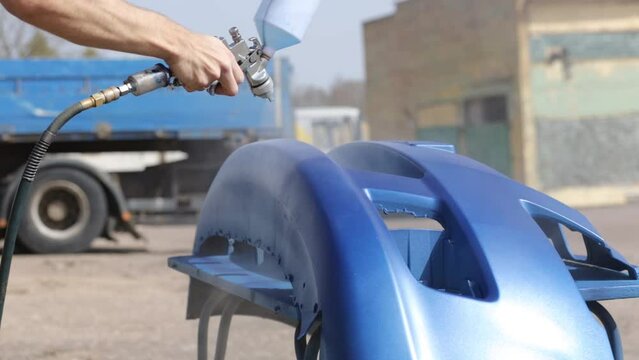 мman spray paints a car bumper blue