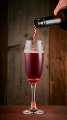 Red wine being poured from bottle to wine glass with a wooden background.