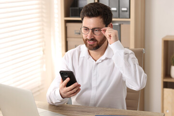 Smiling man using smartphone at table in office