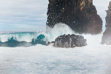 Huge ocean waves crash against coastal rocks against the backdrop on the island of Madeira