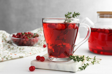 Tasty hot cranberry tea with thyme and fresh berries in glass cup on white wooden table
