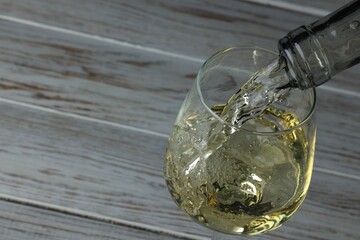 Pouring tasty aromatic wine in glass at wooden table, closeup. Space for text